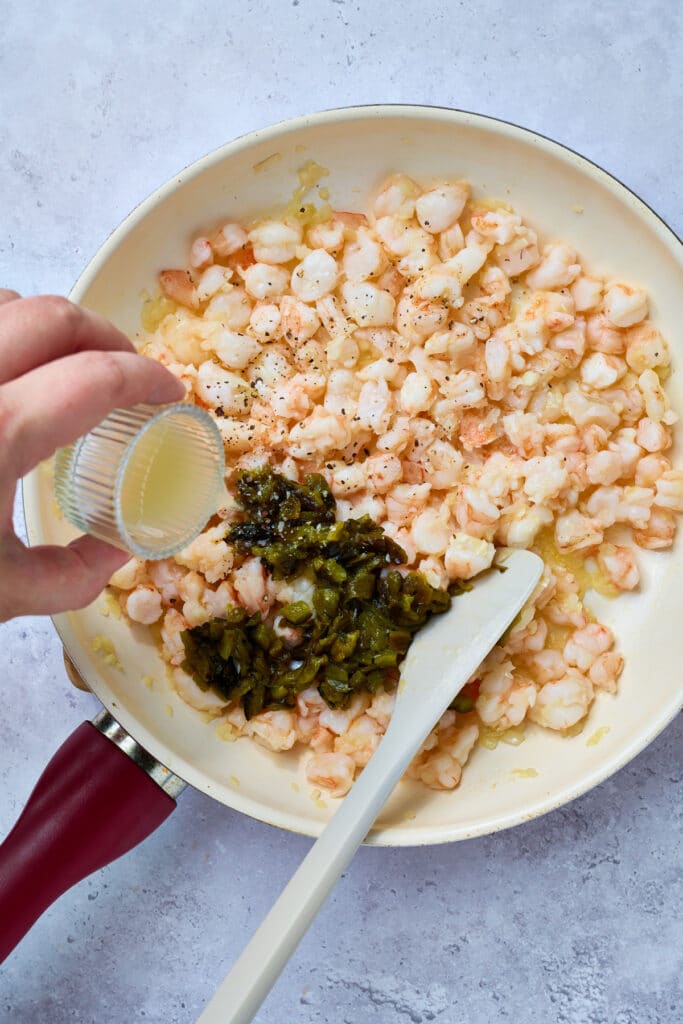 Pouring lime juice into a skillet with sautéed shrimp and chopped, roasted poblano peppers