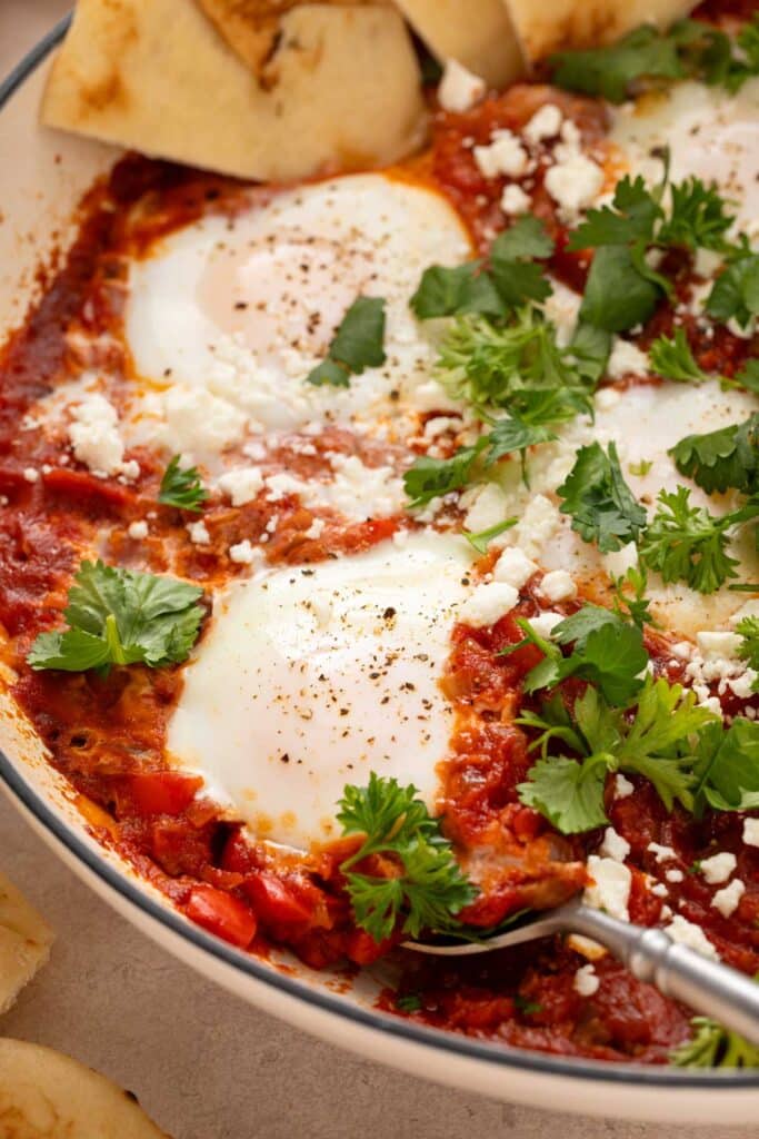 A skillet with a spoon lifting poached eggs in tomato sauce