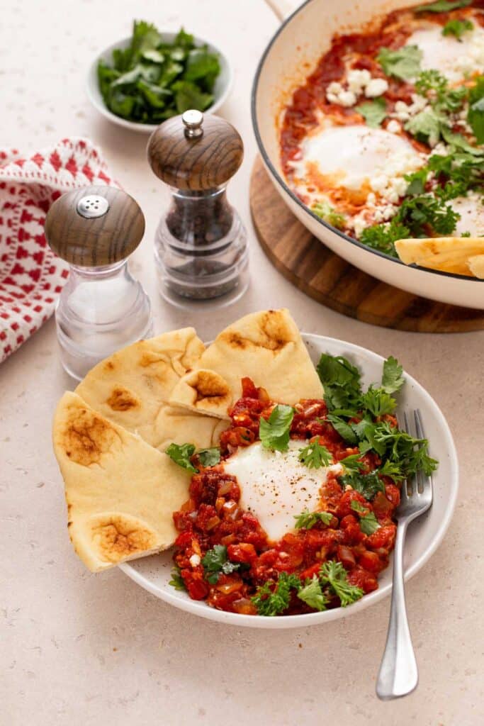 A bowl with eggs in chunky tomato sauce served with pita bread.