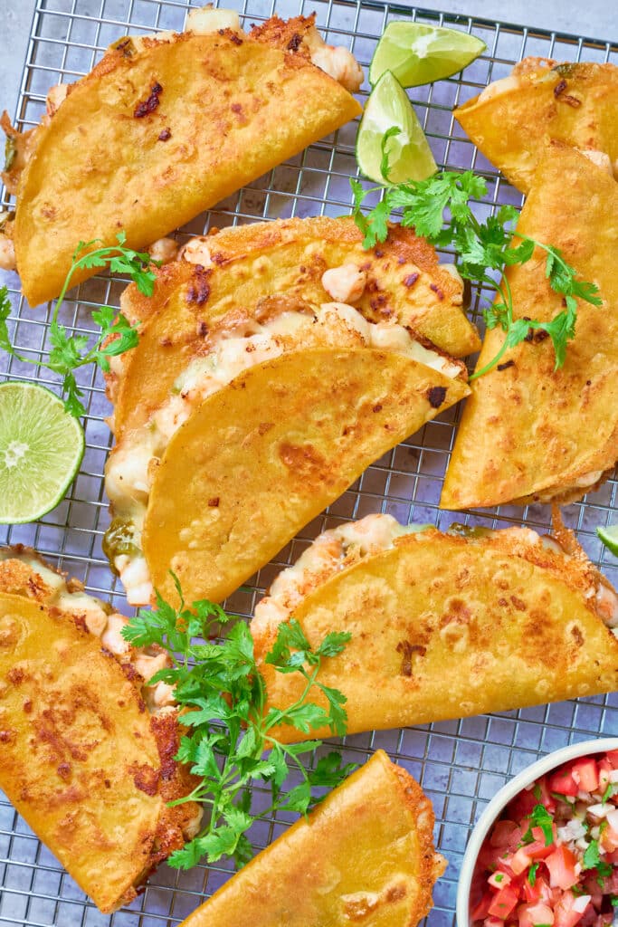 Golden brown crispy tacos on a rack garnished with limes and cilantro