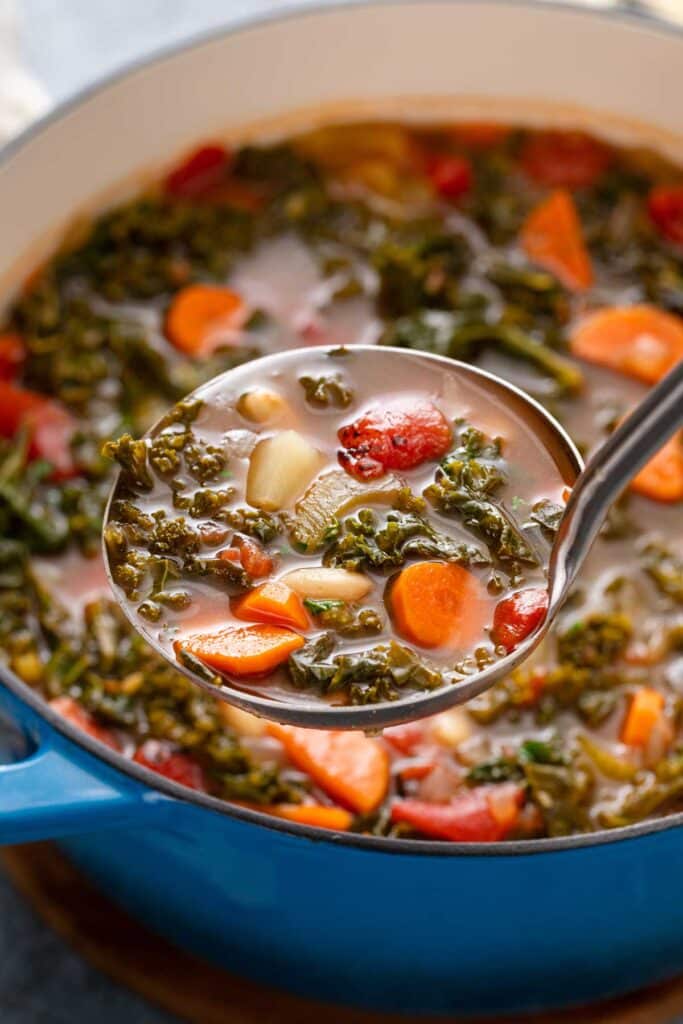 Laddle of white been and hearty greens soup lifted from a pot.