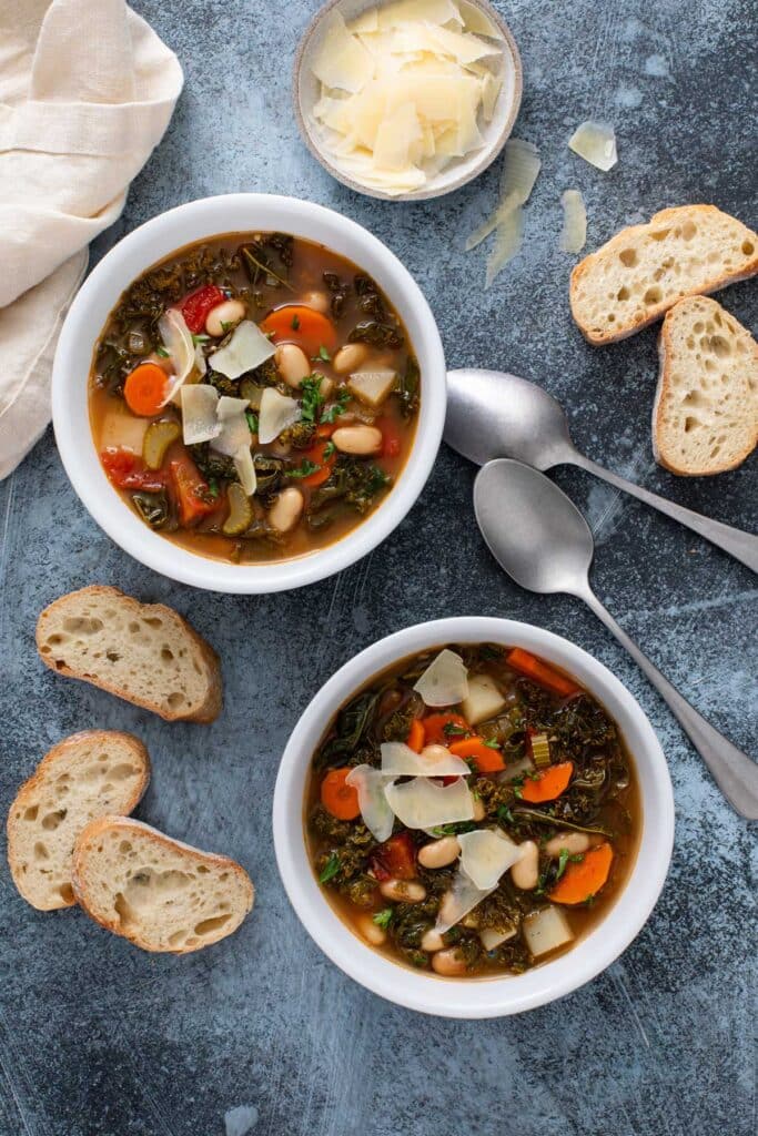 Two bowls of bean and vegetable soup and crusty bread next to them