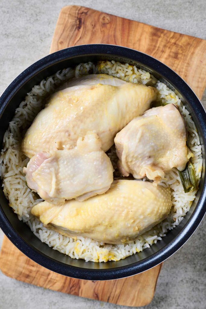 Poached skin on chicken pieces over cooked rice in a rice cooker