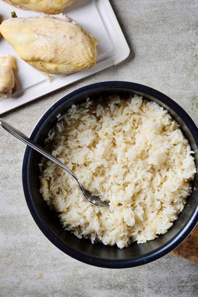 Rice cooker with fluffy rice next to a plate of poached chicken