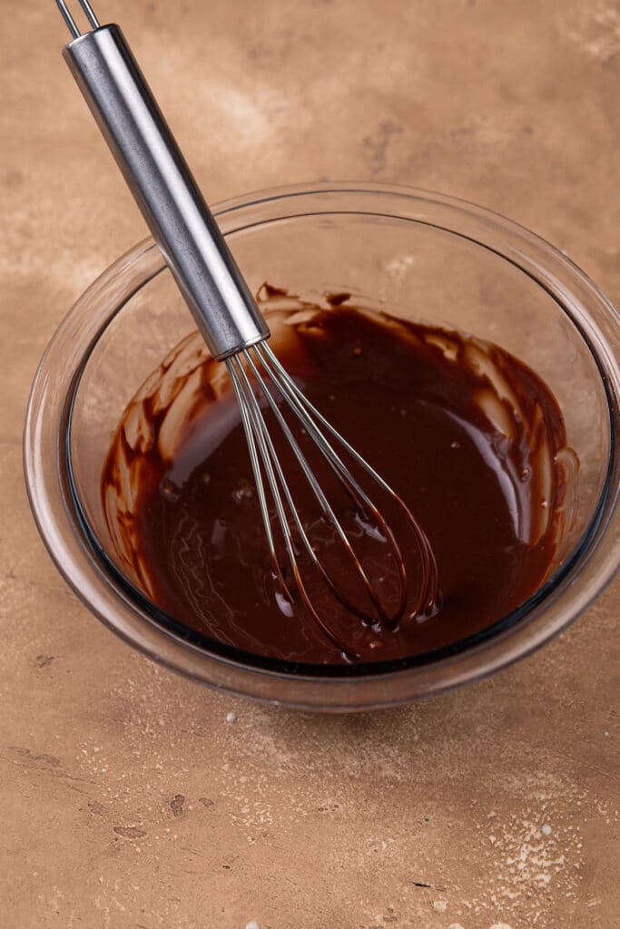 chocolate ganache in a clear bowl with a whisk