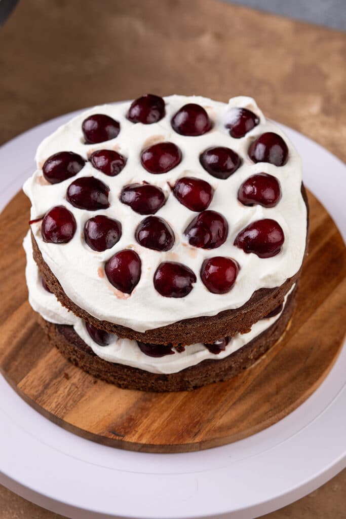 assembling the layers for the black forest cake with whipped cream and cherry halves