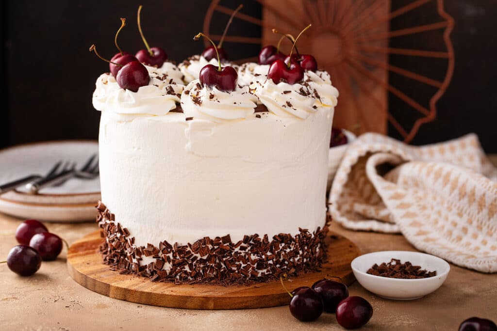 a whole Black Forest Cake with whipped cream frosting and decorated with dark chocolate shavings and whole cherries on top
