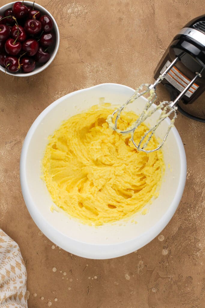 Creamed butter in a mixing bowl next to an electric mixer