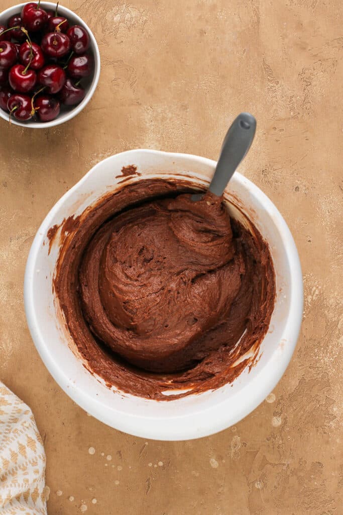 black forest cake batter in a white bowl and a spatula