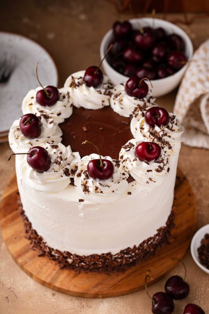 Top view of a black forest cake topped with chocolate ganache, whipped cream and fresh cherries.