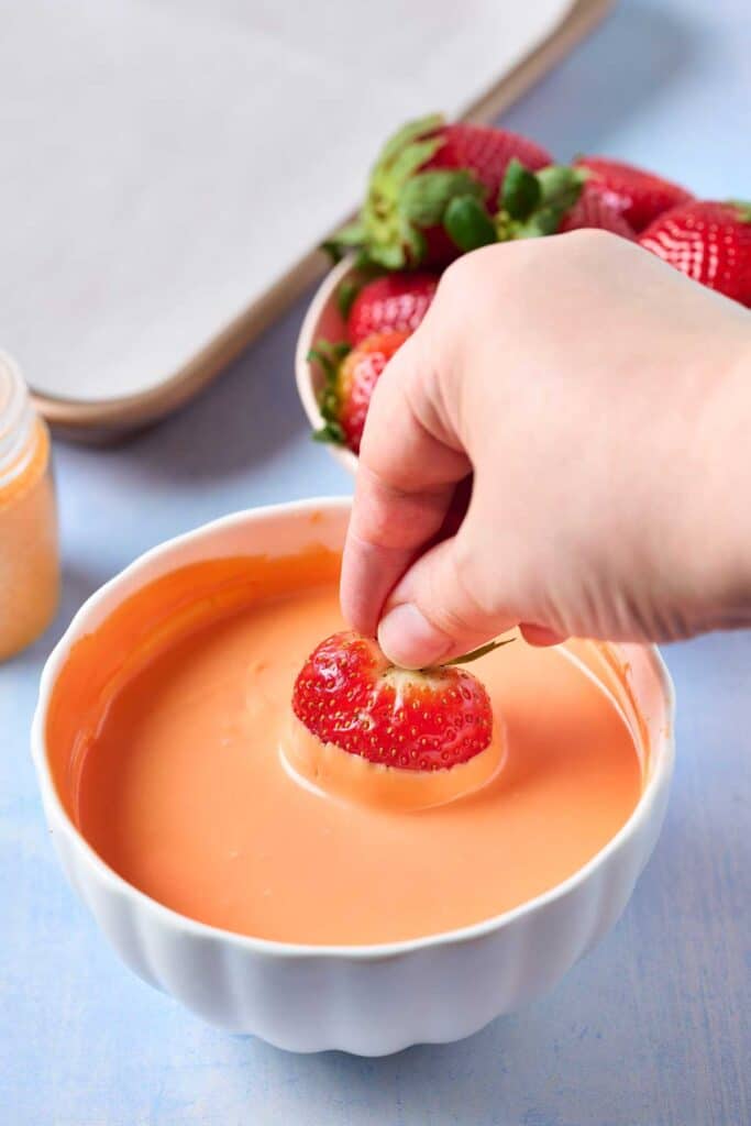 Dipping a strawberry in melted orange candy melts