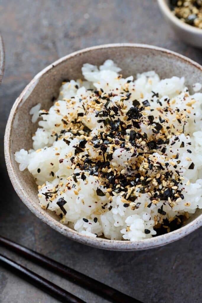 A bowl of white steamed rice topped with a healthy sprinkle of furikake rice seasoning.