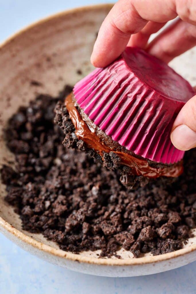 Dipping a chocolate ganache covered chocolate cupcake into Oreo crumbs