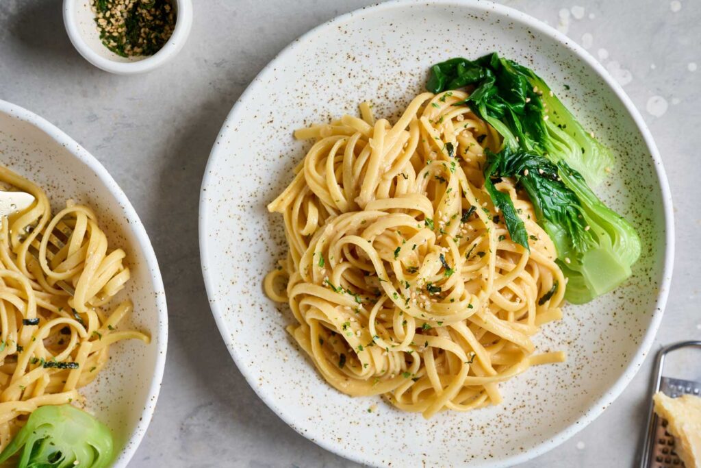 Two bowls with spaghetti tossed in miso sauce served with bok choy