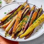 A plate of roasted whole rainbow carrots garnished with chopped parsley