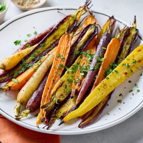 A plate of roasted whole rainbow carrots garnished with chopped parsley