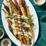 A plate with roasted rainbow carrots topped with gremolata and drizzled with tahini sauce