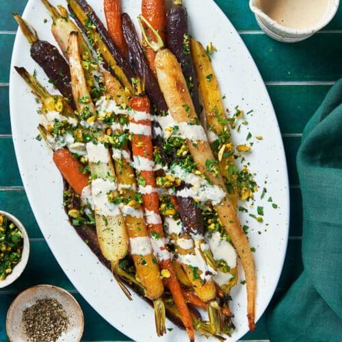 A plate with roasted rainbow carrots topped with gremolata and drizzled with tahini sauce