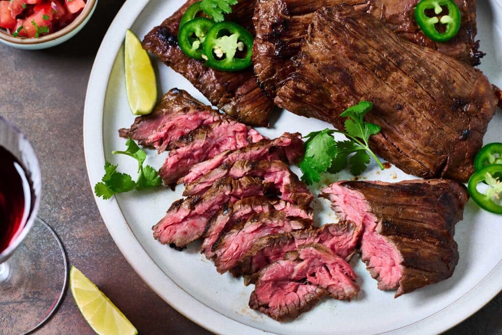 Sliced marinated skirt steak next to bigger pieces of steak on a plate