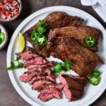 Grilled skirt steak serve with lime wedges, jalapeno slices and cilantro