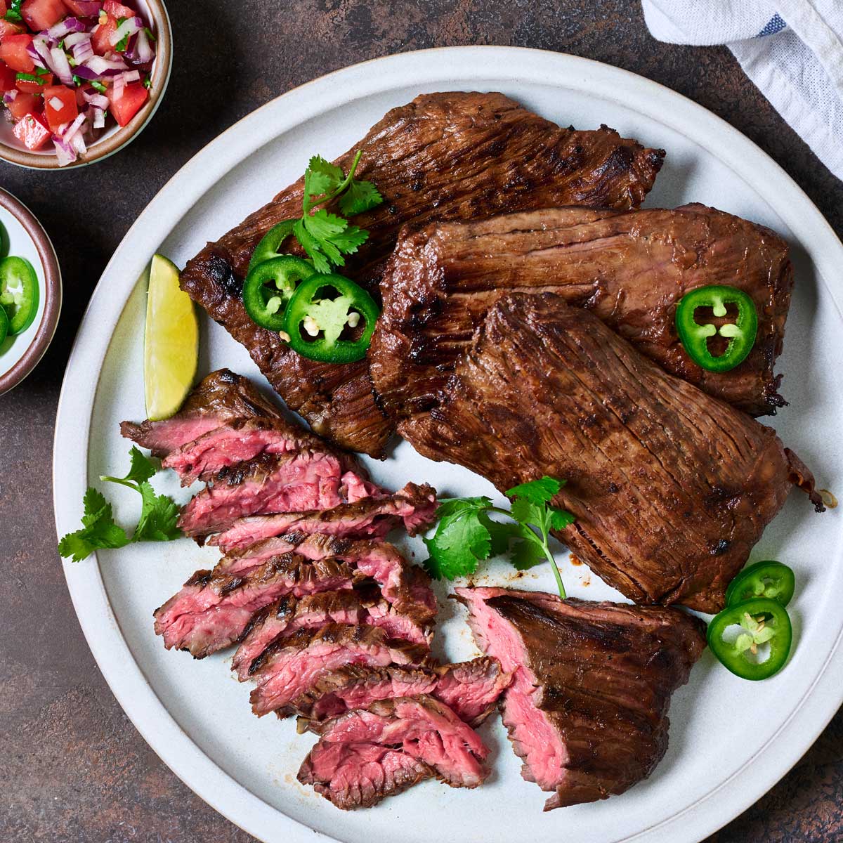 Grilled skirt steak serve with lime wedges, jalapeno slices and cilantro