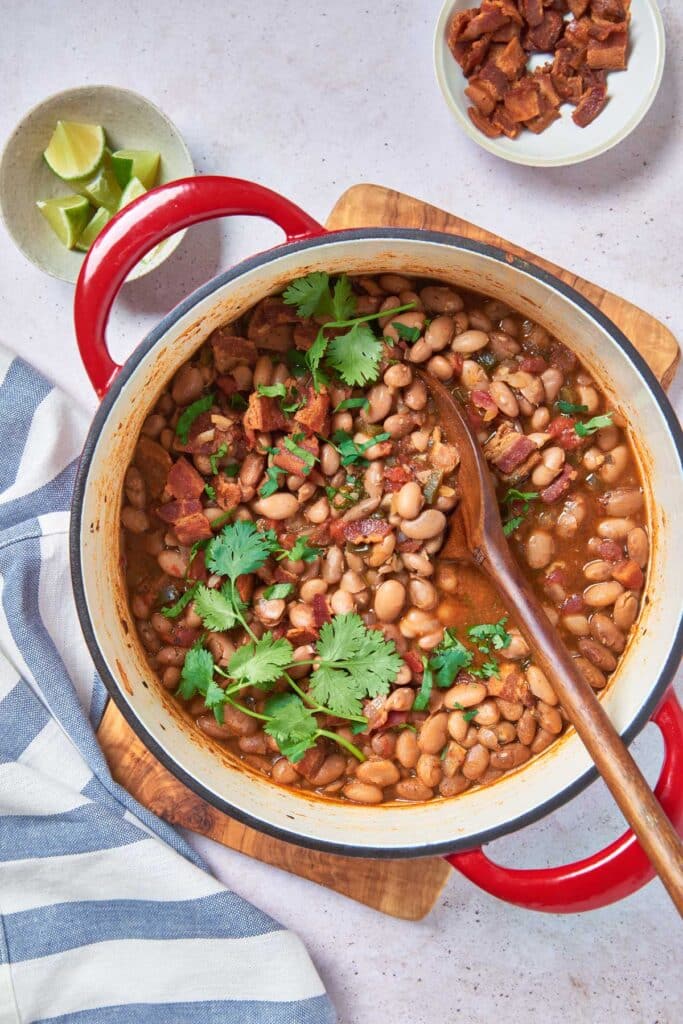 top view of a pot of tender pinto beans with bacon and cilantro with a wooden spoon in it