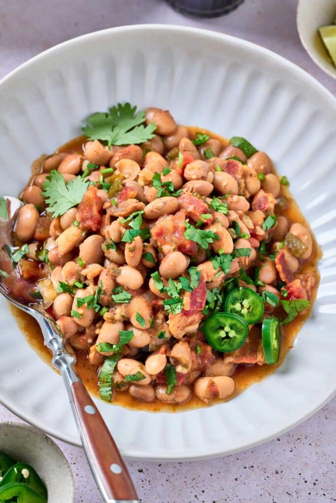 Pinto beans stewed with tomatoes and cripy bacon and topped with cilantro on a plate