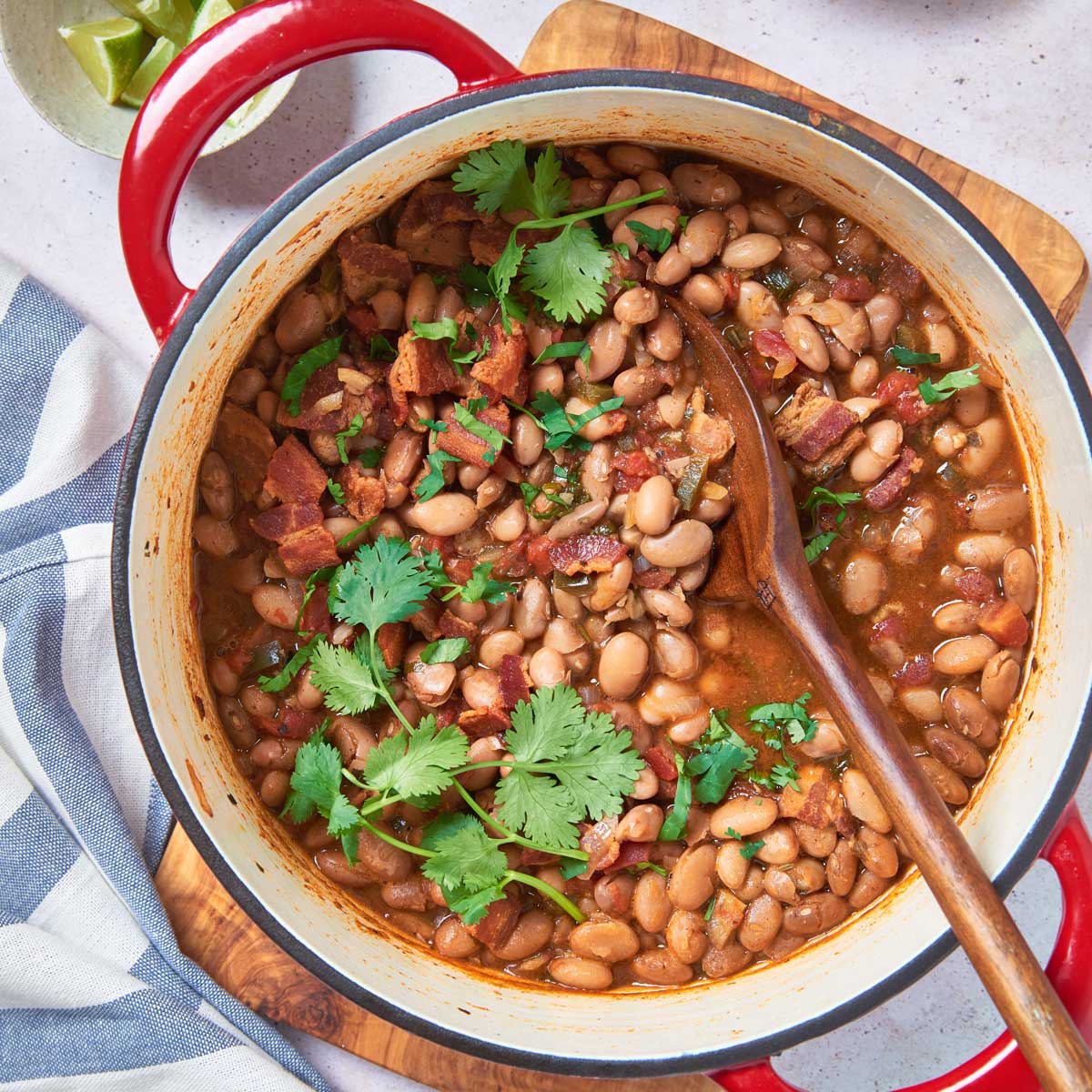 A Dutch oven filled with Mexican pinto beans with tomatoes, cilantro and crispy bacon