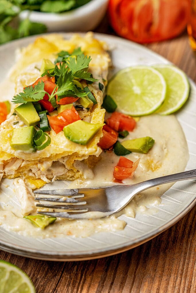 A plate with achicken cheese enchilada covered in a creamy sauce and topped with tomatoes and avocado