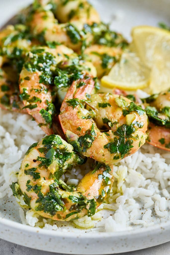 Large shrimp with tails cooked with garlic herb chimmichurri over. bed of white rice and garnish with lemon slices