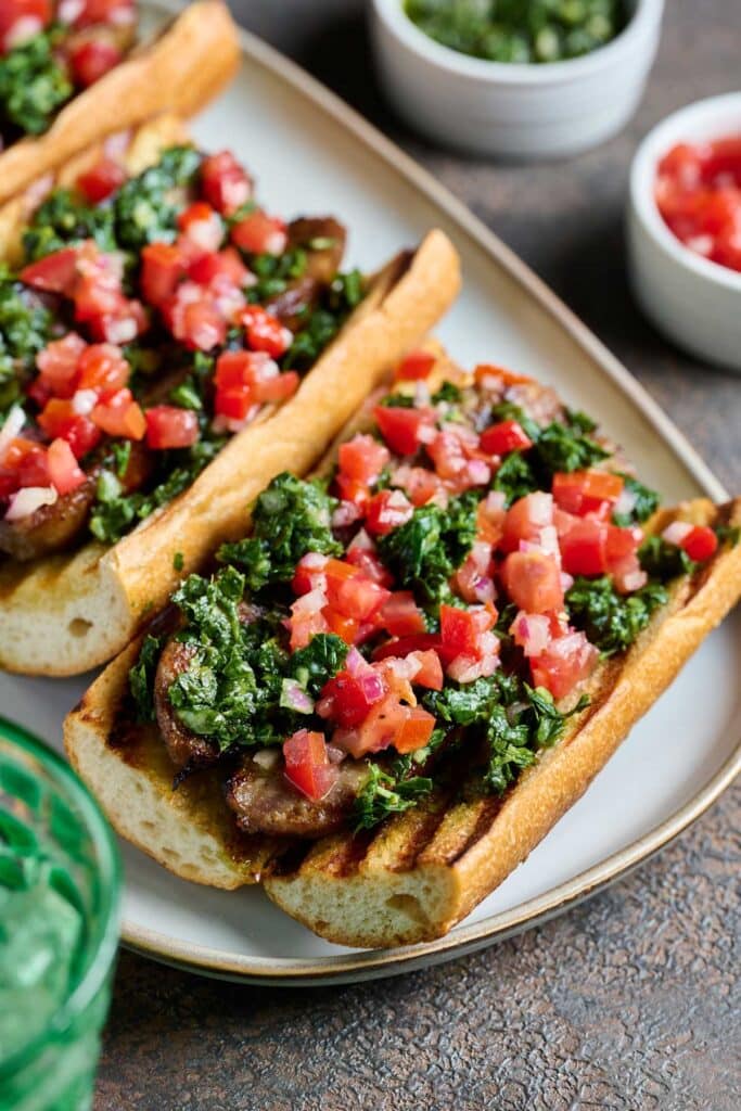 Closeup view of sausage sandwiches topped with tomato salsa and herb chimichurri