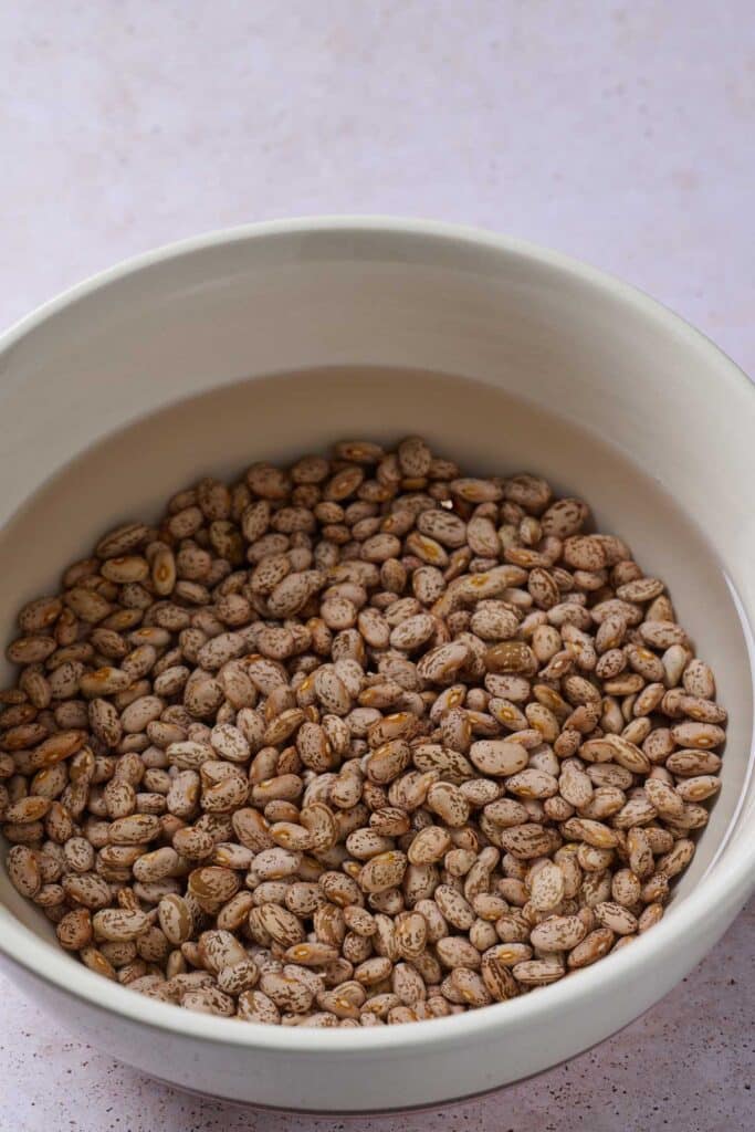 Soaking pinto beans in water in a large ceramic bowl.