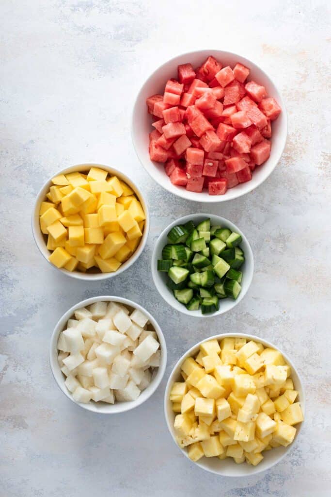 Small bowls of diced fruit, watermelon, mango, cucumber, jicama and pineapple.