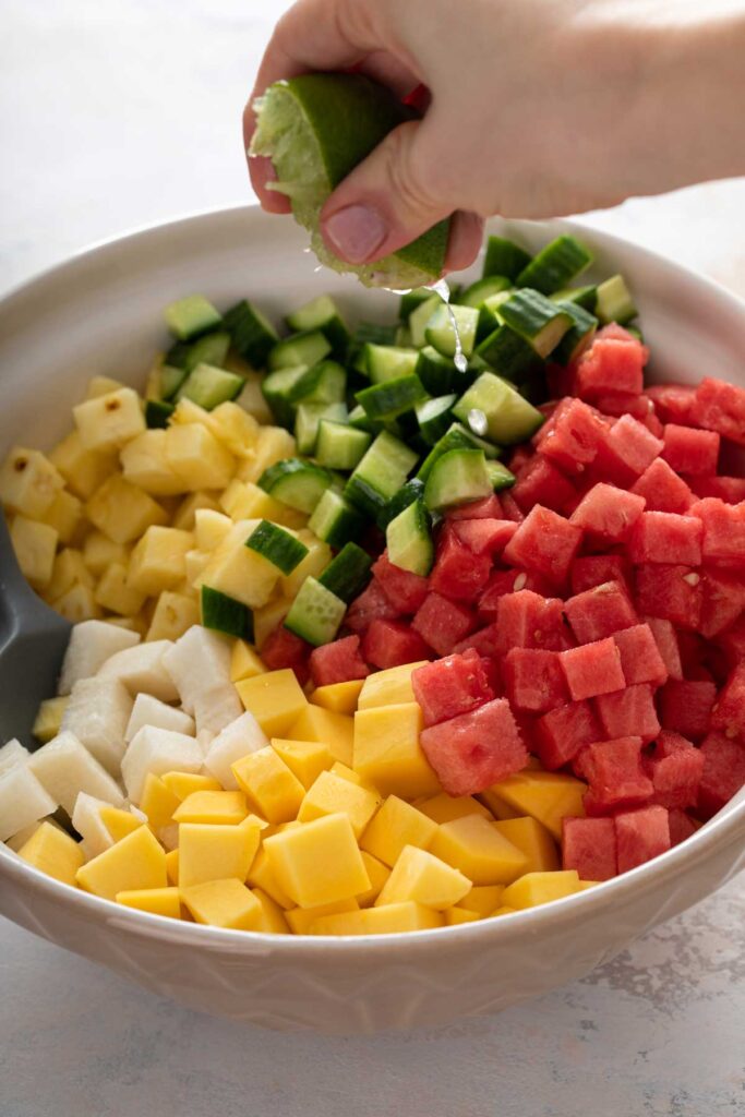 Squeezing lime juice over a bowl of chopped fruit