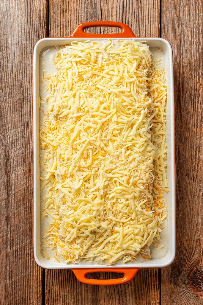 A baking dish with enchiladas and shredded cheese