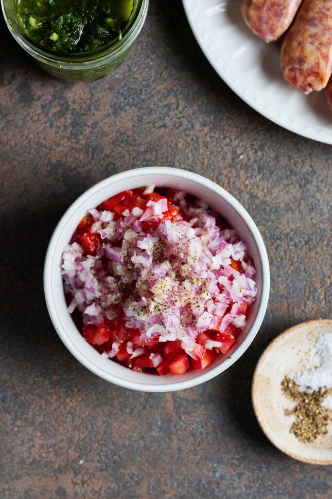 Chopped tomatoes, bell peppers and onion in a bowl seasoned with salt and pepper