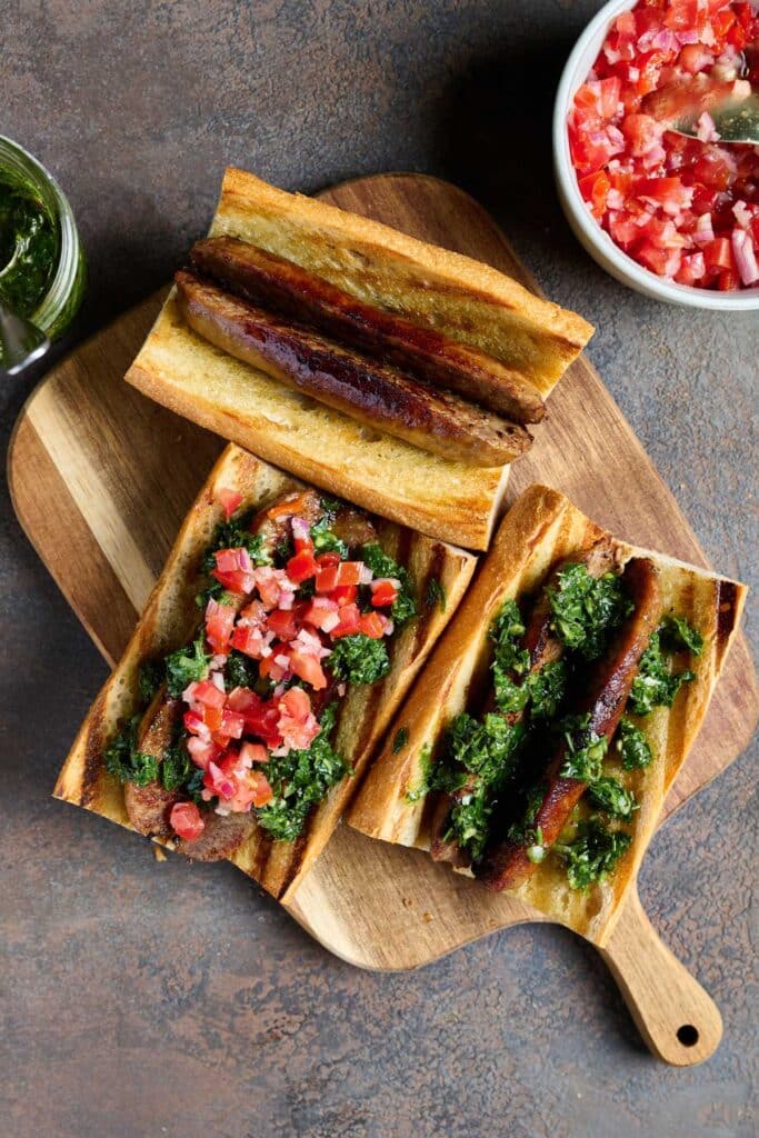 grilled bread topped with golden brown sausage butterflied . Some sandwiches are topped with tomatoes and herb sauce