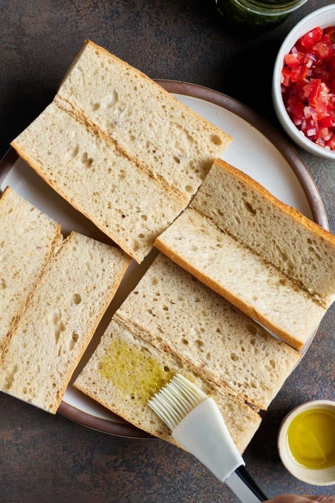 French bread pieces getting brushed with olive oil