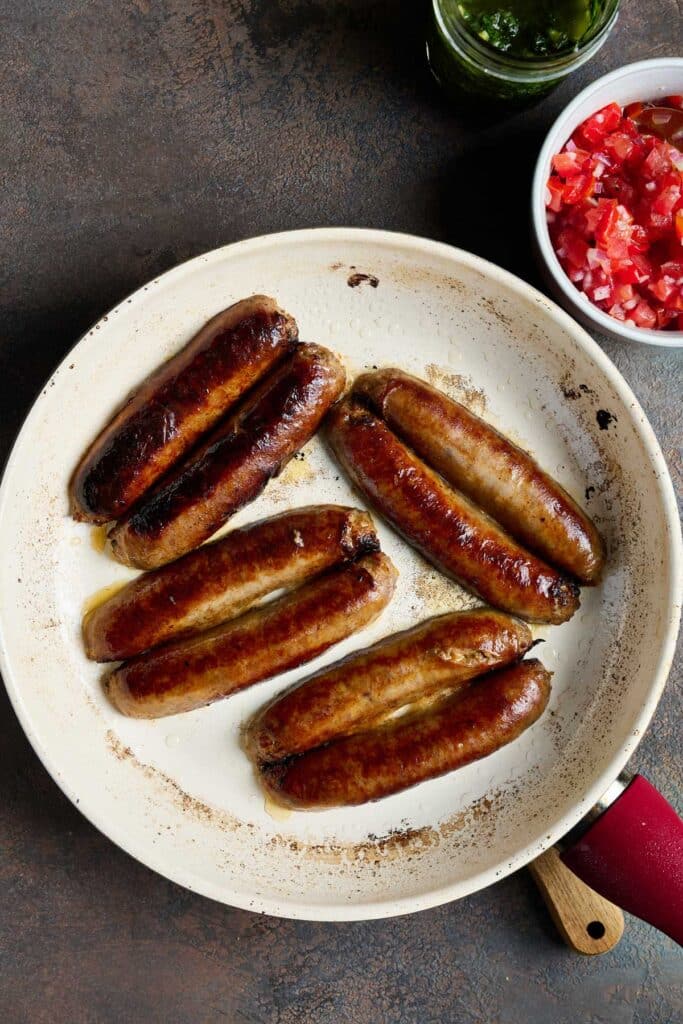 Sausages cut in half lengthwise cooking in a skillet