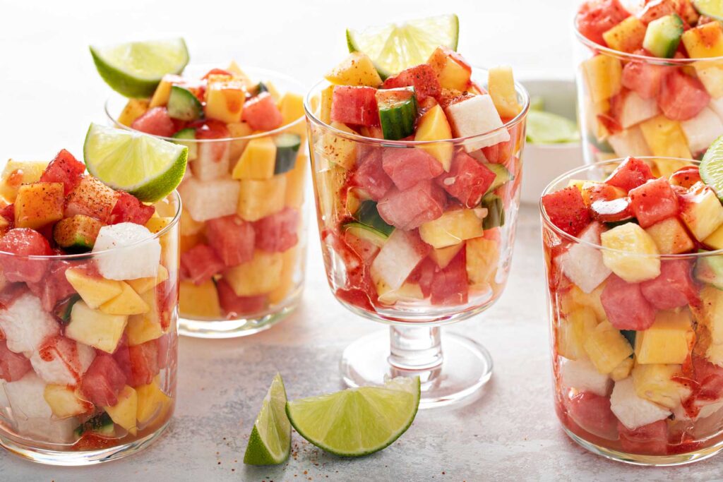 Several cups filled with chopped fruit, garnished with lime wedges