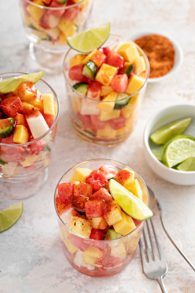 Cups filled with chopped fruit pieces seasoned with tajin and chamoy sauce