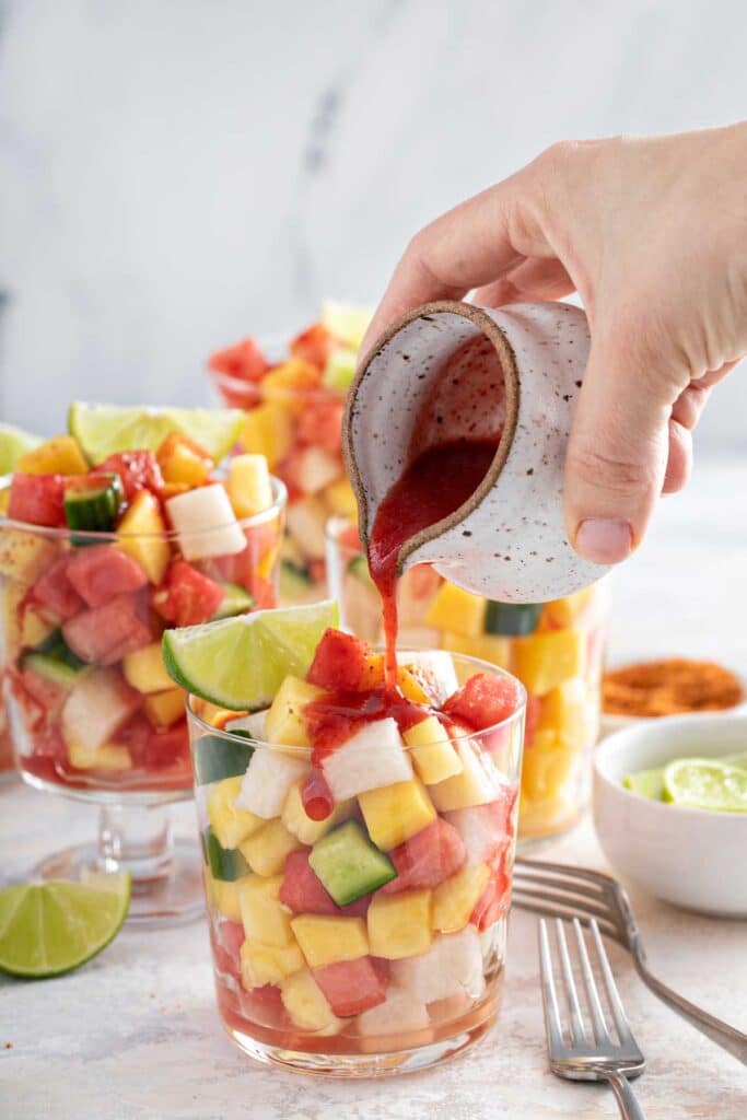 Pouring Mexican chamoy sauce over a cup of fresh fruit