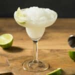 A glass filled with frozen margarita garnished with a lime wedge