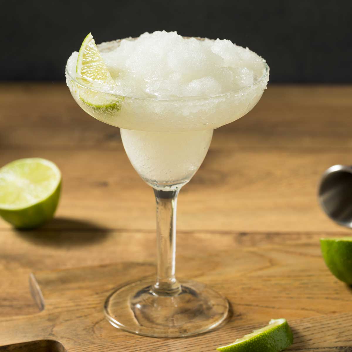 A glass filled with frozen margarita garnished with a lime wedge