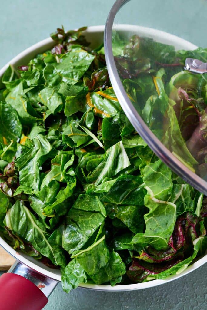 Putting a lid on a skillet filled with fresh chard
