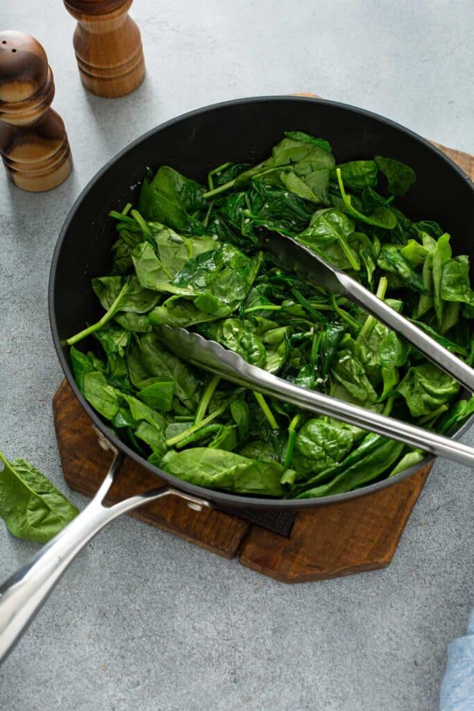 Tossing baby spinach in garlic oil in a skillet