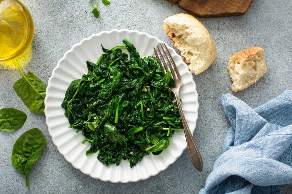 A white fluted plate with sauteed baby spinach with garlic on a light gray counter