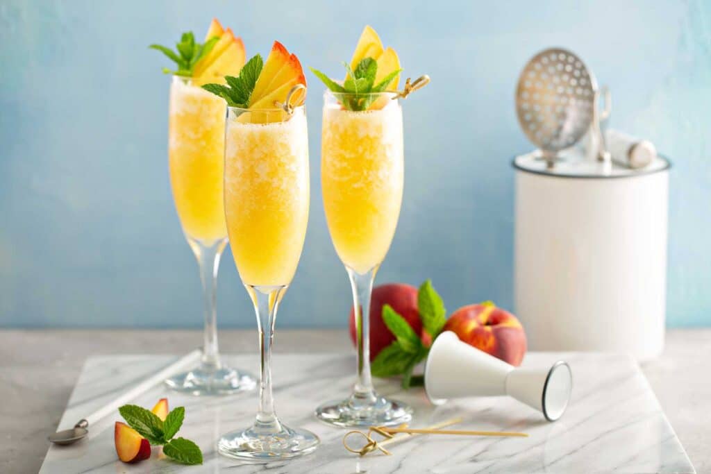 Flute glasses filled with peach cocktail garnished with fresh peach slices