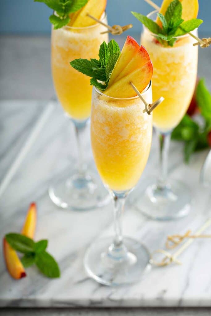 Peach Bellini cocktail served in a champagne flute with fresh peach slices and mint garnish