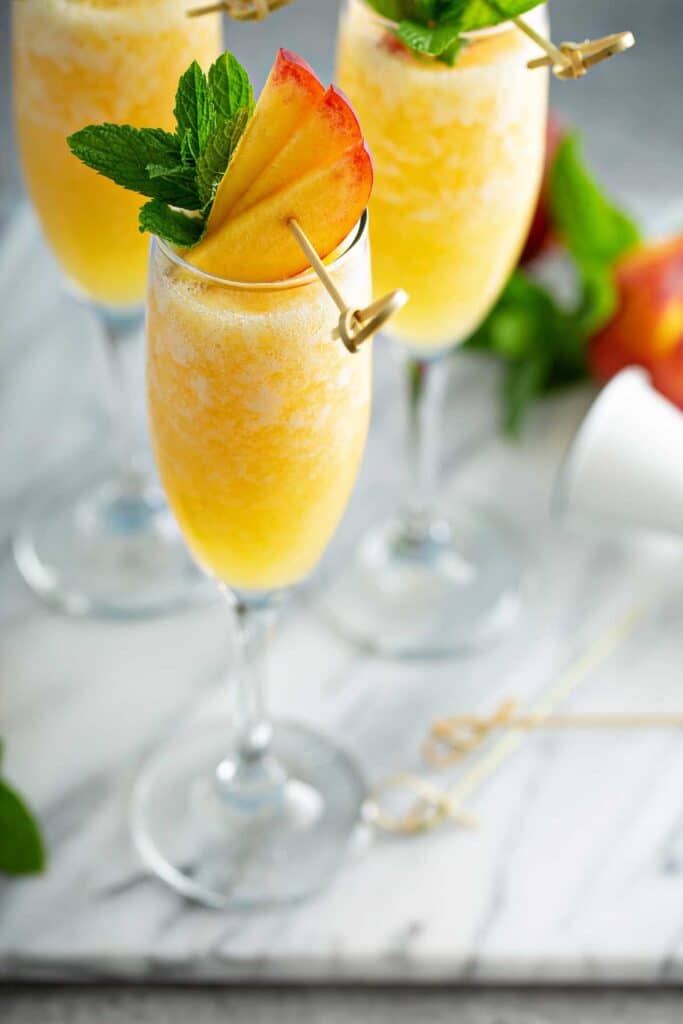 Peach Bellini served in a champagne flute with fresh peach slices and mint garnish